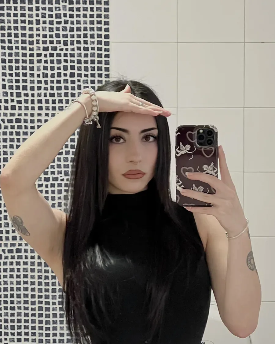 Pilar haciéndose una foto en el espejo, con un top negro y la mano en la frente